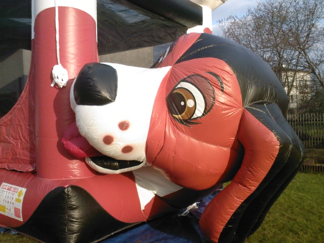 Nadmuchiwany zamek w kształcie głowy psa z wystawionym językiem, widoczne zasady bezpieczeństwa na boku, na trawniku.